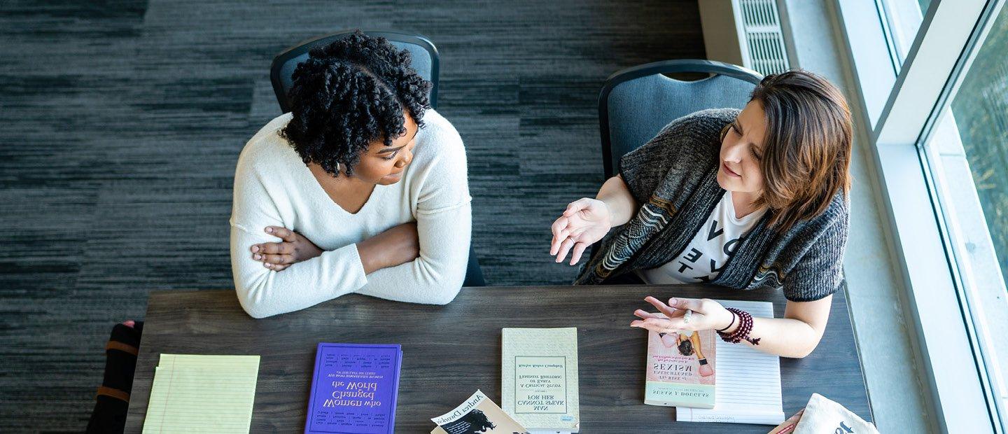 An aerial photo of two women seated at a table with books and notepads.